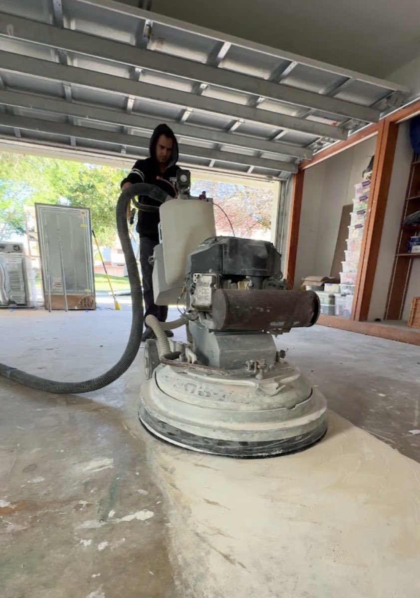 Suncrete Coatings technician diamond-grinding a garage slab in protective gear