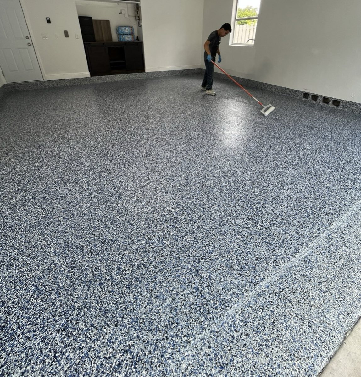 Suncrete Coatings installer rolling out a blue flake epoxy garage floor in Miami Beach, FL